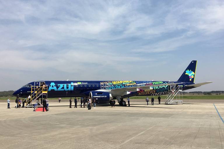 Avião azul escuro com o nome da companhia aérea em azul claro é visto ao fundo, estacionado em um aeroporto