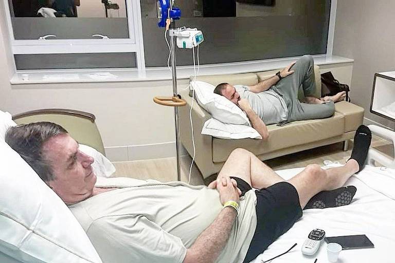 Jair Bolsonaro e o filho Carlos assistem à TV no quarto do hospital onde o presidente se recupera de cirurgia