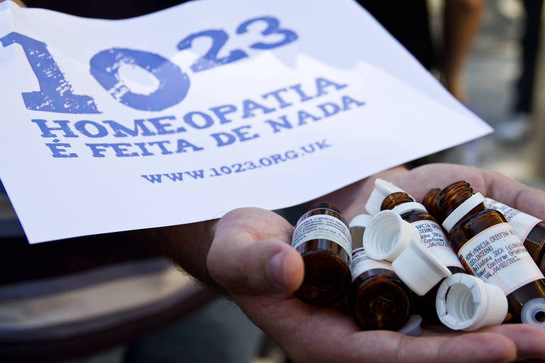 Manifestante carrega frascos vazios de medicamentos homeopáticos e um cartaz que diz: "Homeopatia é feita de nada"