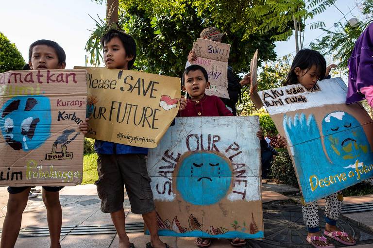 Em Surabaya, grupo de crianças indonésias seguram cartazes com mensagens que pedem que as pessoas salvem o planeta Terra