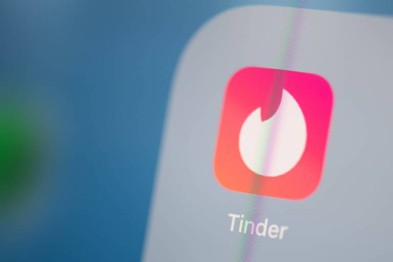 A foto mostra a tela de um celular com um ícone do aplicativo de relacionamentos Tinder, com um foguinho branco em um fundo rosa