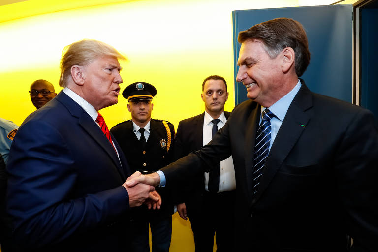 Presidente Jair Bolsonaro cumprimenta Donald Trump com aperto de mãos. Bolsonaro sorri e Trump comenta algo