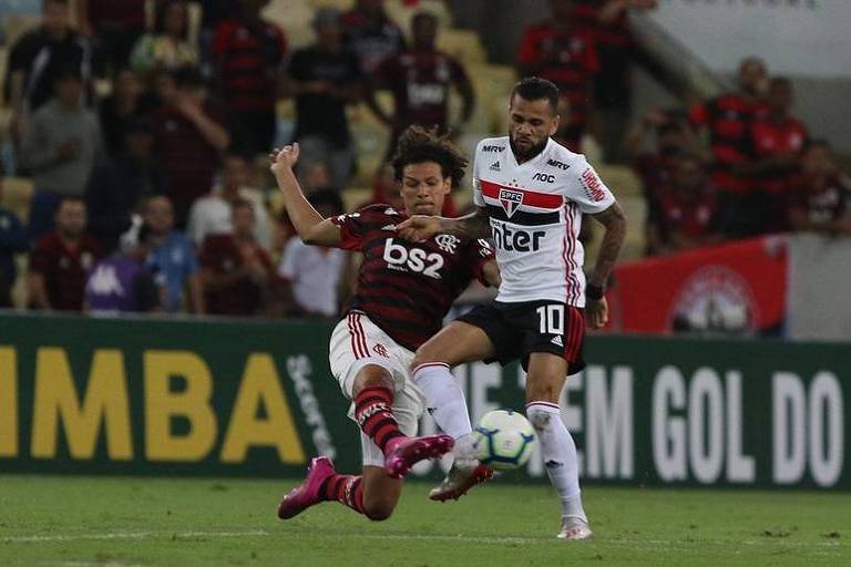 O meia são-paulino Daniel Alves tenta executar um lançamento e é travado pelo volante Willian Arão, do Flamengo