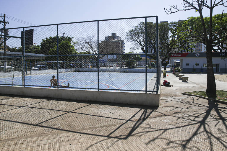 Homem descansa em quadra da praça Princesa Isabel, no centro de São Paulo; do lado de fora, um morador de rua dorme no chão