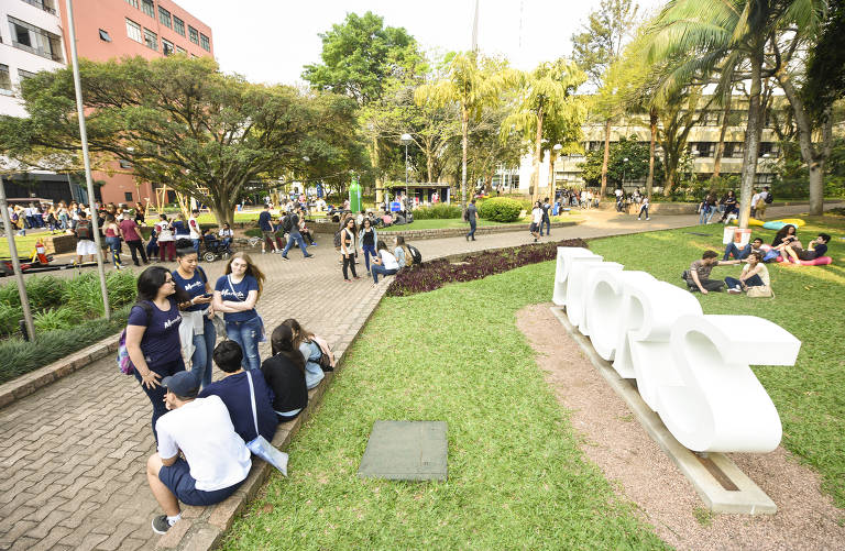 Geral do campus da PUC do Rio Grande do Sul, com letreiro da universidade do lado direito, caminho gramado e vários alunos espalhados