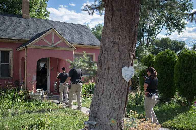 policiais caminham em jardim em direção à porta de frente de uma casa