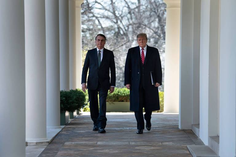 Em um corredor do jardim da casa branca, Jair Bolsonaro e Donald Trump caminham, lado a lado. 
