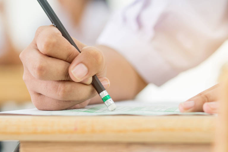 Fotografia colorida mostra mão segurando lápis preto com borracha na ponta