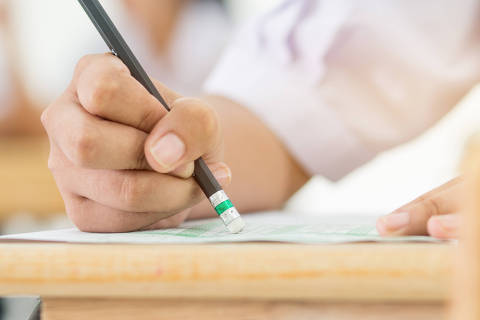 Students holding pencil eraser while taking exams, examination room, writing answer optical form in high school classroom, view of having test in class on seat rows, Education  literacy concept.Credit Smolaw / Adobe Stock