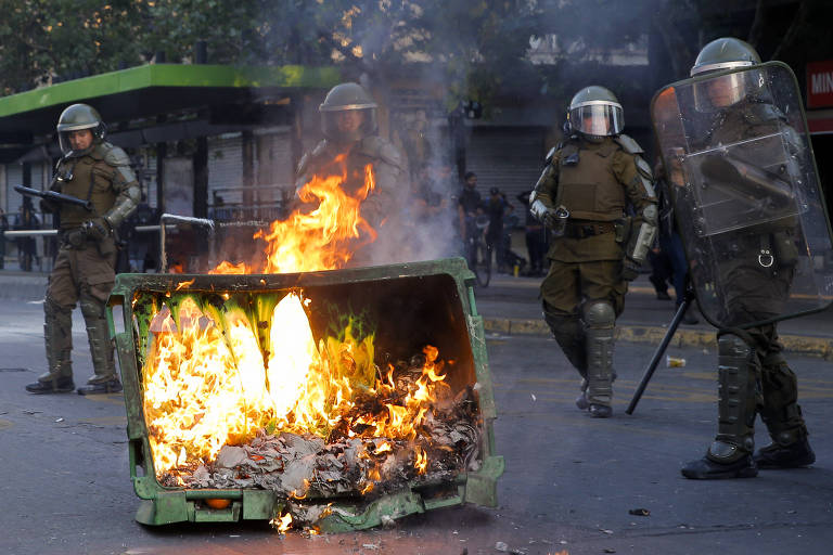 Policiais da tropa de choque ao lado de barricada em chamas em Santiago