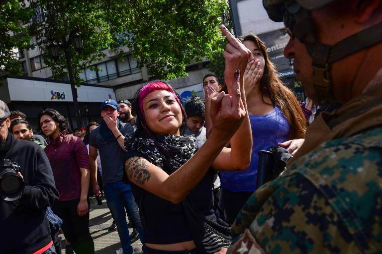 Manifestantes gesticulam para policiais durante ato em Santiago neste sábado (19)