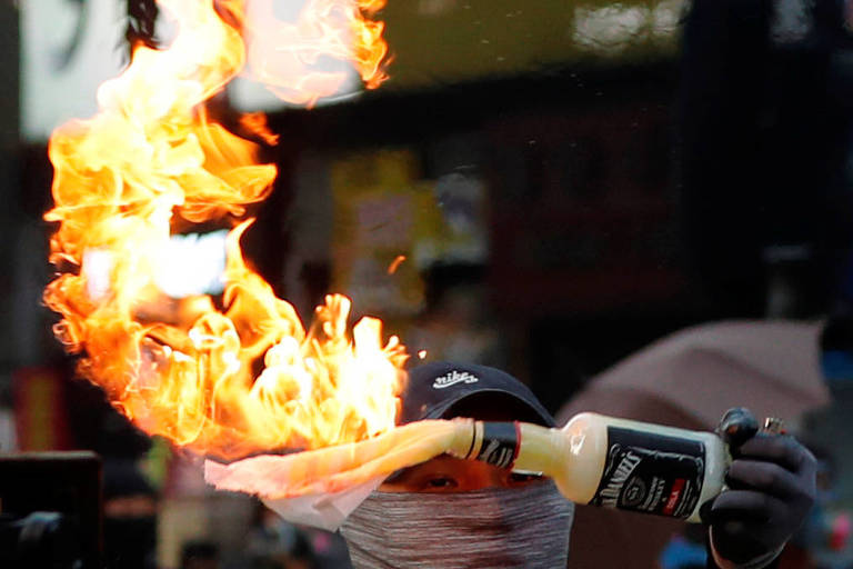 Homem de boné e máscara segura um coquetel molotov, que é uma garrafa com um pano em chamas
