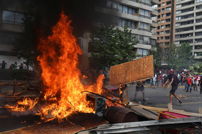 Manifestante joga pedaço de madeira em direção à uma barricada pegando fogo durante protesto em Santiago