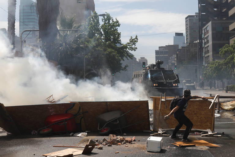 Manifestante joga pedra em direção à carro de guerra da polícia em Santiago