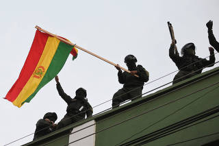 Police officers wave a national flag while standing on the roof of their headquarters, in Cochabamba