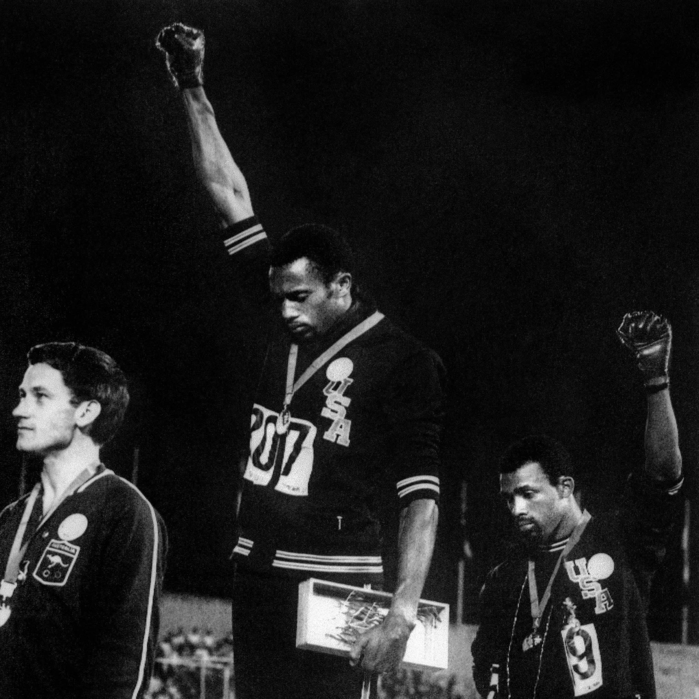 Os atletas negros Tommie Smith (centro) e John Carlos (dir.), medalhas de ouro e de bronze nos 200 m, fazem a saudação com o punho cerrado do grupo Panteras Negras, como protesto a conflitos raciais nos EUA