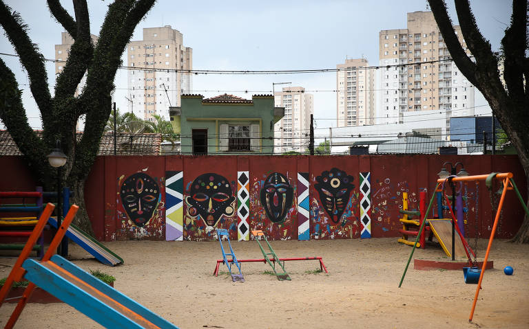 Ao fundo, imagens da cultura africana estampam muro de escola infantil; em sua frente, é possível ver o parquinho da instituição