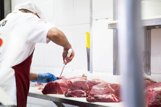 Açougueiro manipula peças de carnes em estabelecimento comercial especializado
