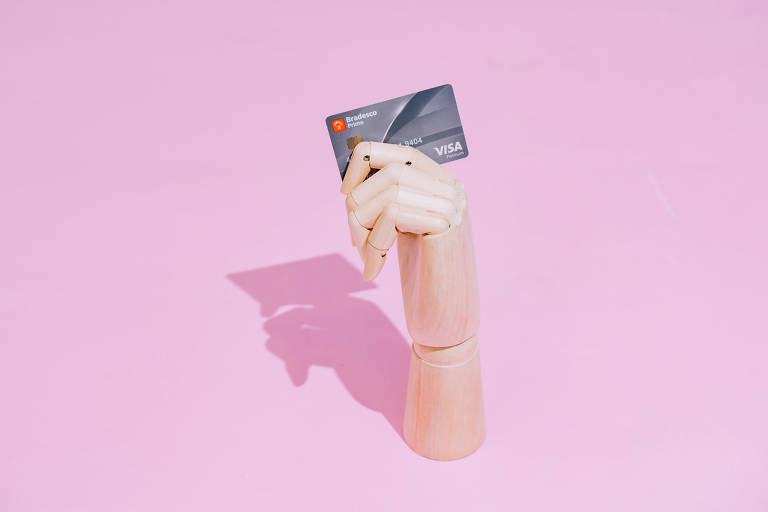 Mão segurando um cartão de crédito em um fundo rosa