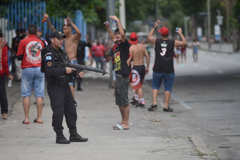 Homem ergue os braços próximo a policial armado durante confusão na festa que reuniu torcedores rubro-negros