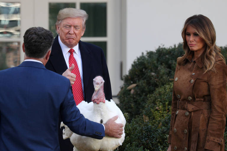 O presidente dos Estados Unidos, Donald Trump, faz"joinha" para um dos perus ganhadores do "72nd National Thanksgiving Turkeys". Ao seu lado, a primeira dama, Melania Trump, observa a ação.