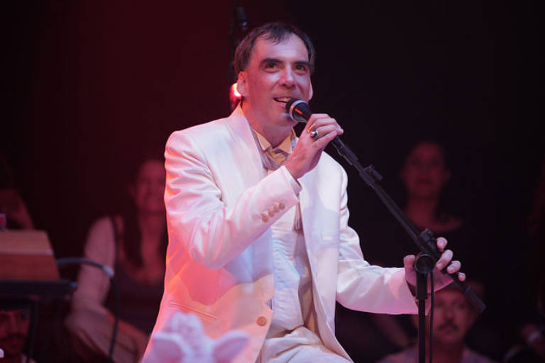 Arnaldo Antunes, vestido de branco, segura microfone em show