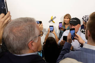A woman poses for a photo next to a banana attached with duct-tape that replaces the artwork 'Comedian' by the artist Maurizio Cattelan, which was eaten by David Datuna, in Miami Beach