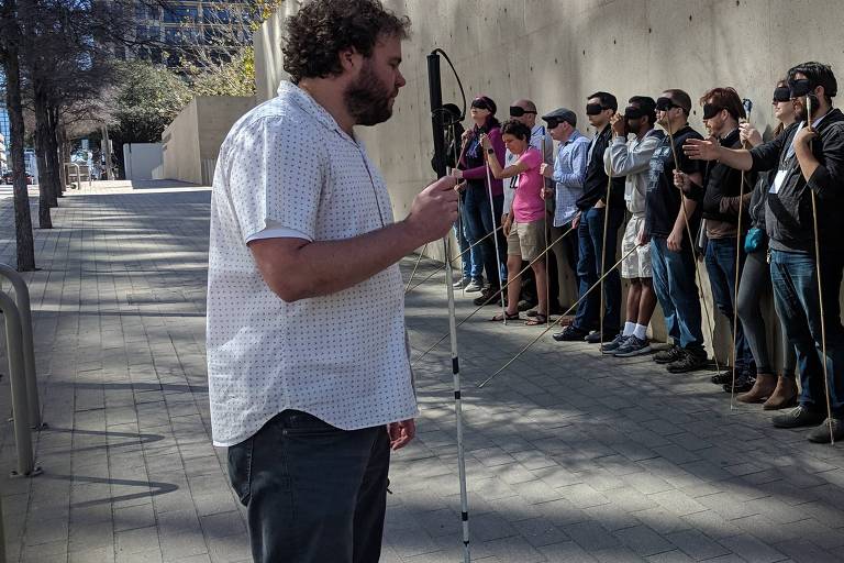 O educador Brian Bushway, um californiano de 36 anos e o único cego na turma, lidera grupo de 20 pessoas pelas ruas de Austin com os olhos vendados e com uma bengala de bambu em mãos;