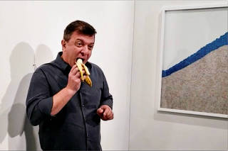 David Datuna eats a banana that was attached with duct tape to a wall, which is an artwork titled 'Comedian' by the artist Maurizio Cattelan, in front of a crowd at Art Basel in Miami Beach
