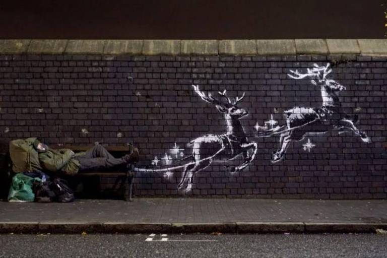 Homem deitado em banco ao lado de grafite de Banksy em Birmingham