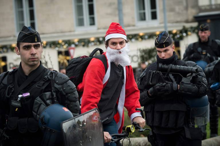 Homem vestido como Papai Noel anda de bicicleta em meio a policiais durante protesto contra projeto da Previdência em Nantes, França