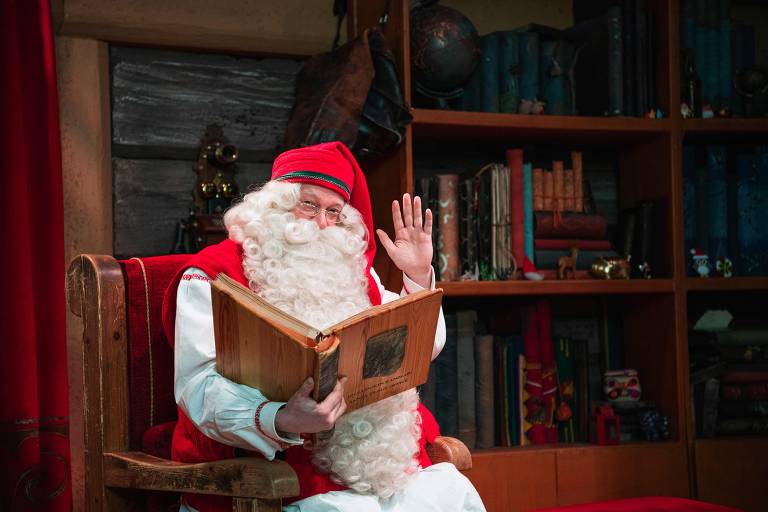 Homem vestido de Papai Noel acena de seu escritório em parque temático na Lapônia