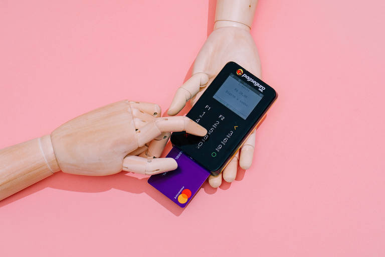 mãos seguram máquina e cartão de crédito em fundo rosa