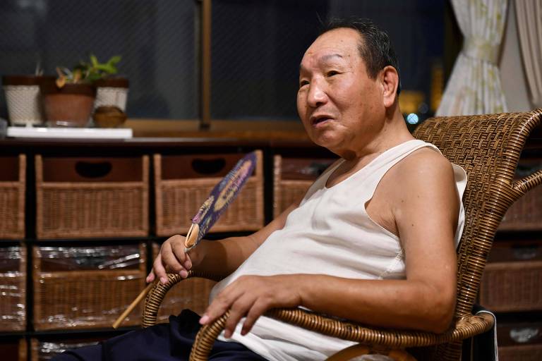 O ex-boxeador profissional chamado Iwao Hakamada aparece sentado em uma cadeira de palha segurando um leque na mão direita.