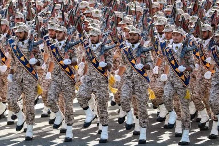 militares marcham em parada, trajam uniforme camuflado na cor  terrosa e calçados brancos com a sola preta