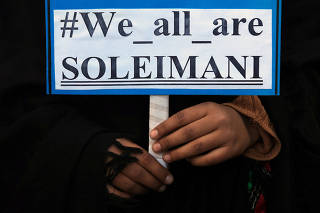 A woman holds a sign with others during a protest over the death of Iranian Major-General Qassem Soleimani, who was killed in an air strike near Baghdad, in Peshawar,