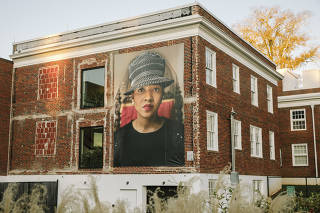 A banner portrait of Brittany, a local resident, is displayed on the exterior of a building near downtown as part of photographer Mary Beth Meehan?s ?Seeing Newnan? art installation project in Newnan, Ga., Nov. 1, 2019. (William Widmer/The New York Times)