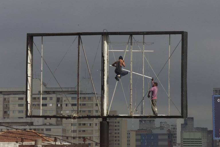Funcionários trocando lâmpadas por mais econômicas em um outdoor luminoso na zona leste de São Paulo