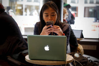 FILE PHOTO: A woman uses her Apple iPhone and laptop in a cafe in lower Manhattan in New York City