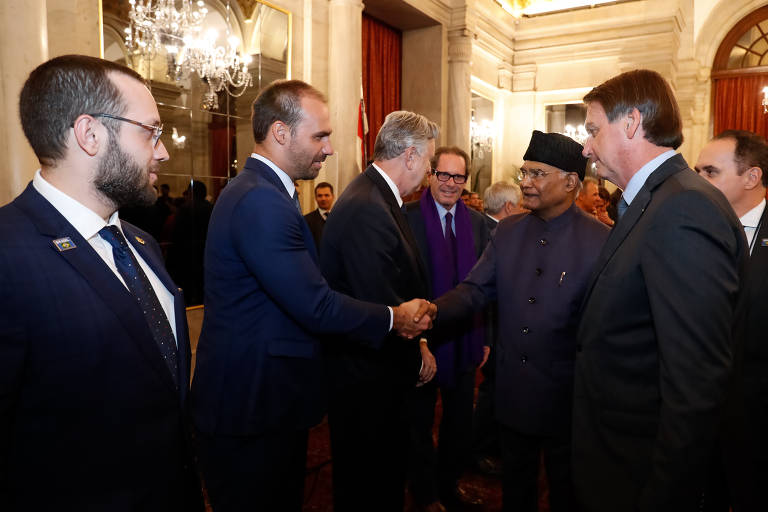 Acompanhado pelo deputado Filipe Barros (PSL) e pelo presidente Jair Bolsonaro, o deputado Eduardo Bolsonaro cumprimenta o presidente da Índia, Ram Nath Kovind, em jantar realizado no sábado (25). No domingo (26), Eduardo defendeu a abertura do mercado de armas brasileiro e foi rebatido pelo presidente da Taurus, que detém o monopólio virtual da fabricação de armas no Brasil