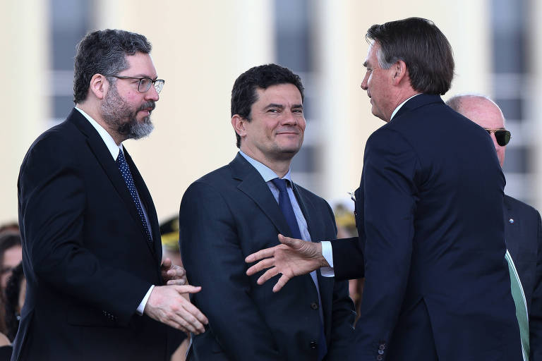 Araújo, à esquerda, estende a mão para Bolsonaro, à direita. Moro está no meio dos dois e sorri