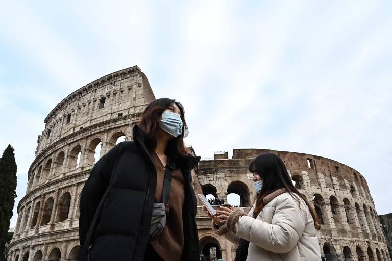 Turistas com máscaras na frente do Coliseu, em Roma