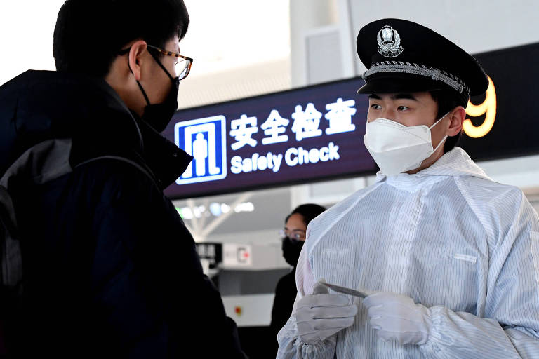Um policial mascarado e de jaleco branco checa a identidade de um passageiro mascarado vestido todo de preto 