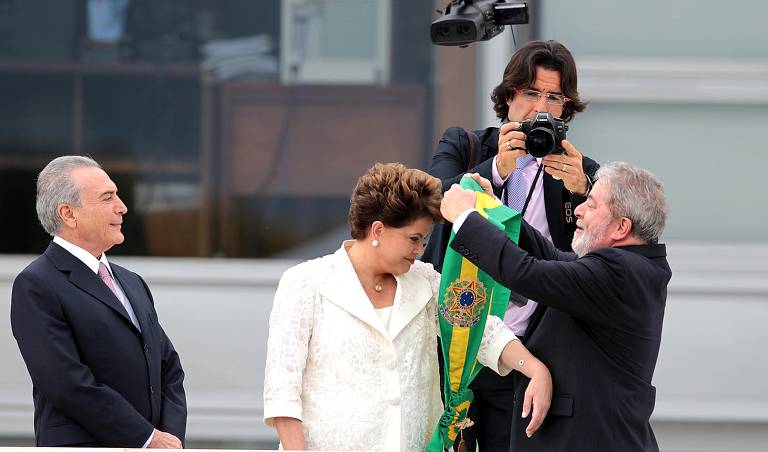 Lula entrega a faixa presidencial à Dilma Rousseff durante a cerimônia de posse na rampa do palácio da Alvorada. À dieita, o vice-presidente Michel Temer