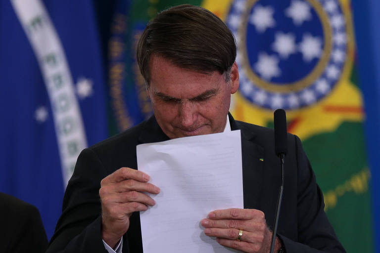 Jair Bolsonaro, sem óculos, tenta ler um papel aproximando-o do rosto