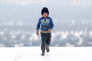 An internally displaced girl walks on snow at a makeshift camp in Azaz