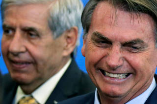 Brazil's President Jair Bolsonaro reacts next to Brazil's Minister of Institutional Security Augusto Heleno during a launch ceremony of real estate credit incentive program of the Caixa Economica Federal Bank at the Planalto Palace in Brasilia