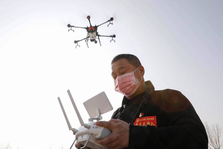 Homem com máscara cirúrgica usa equipamento para operar drone que sobrevoa sobre sua cabeça