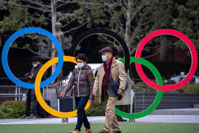Japoneses com máscaras em frente ao Museu Olímpico de Tóquio, no Japão 