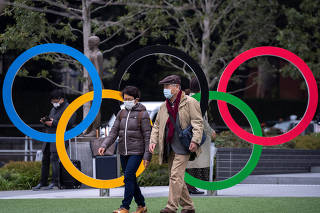 People wearing protective face masks, following an outbreak of the coronavirus, are seen next to the Olympic rings in front of the Japan Olympic Museum in Tokyo
